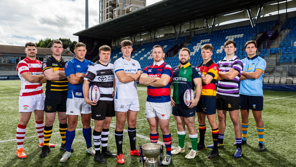 Rugby players in team jerseys standing in a line, trophy in the middle