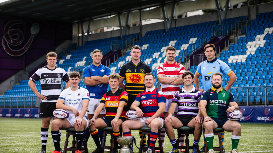 Rugby players in team jerseys, some sitting on chairs, others standing in a line, pose for a group photo.